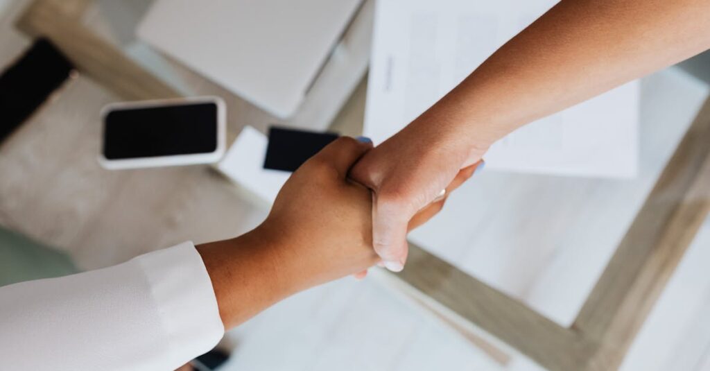 Two people shaking hands over a desk with modern tech, symbolizing a successful business agreement.