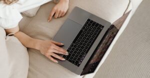 Close-up of a person working from home on a laptop, comfortable on a beige couch.